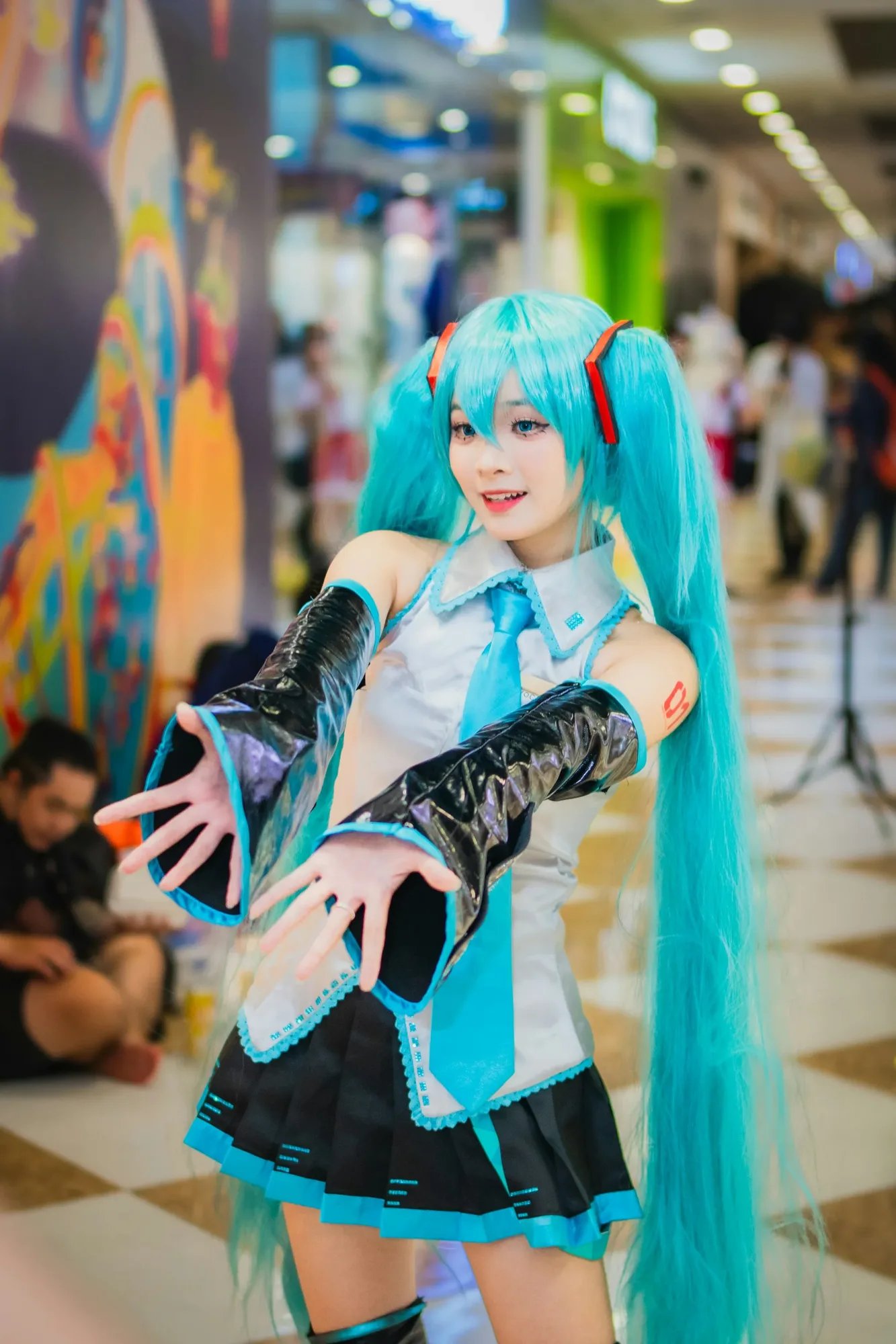 Cosplayer with long blue twin-tail hair posing at a convention.